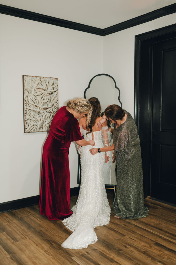 Brides mom and sister helping her put her dress on. 
